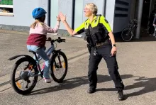 Eine Polizistin schlägt sich mit einem Kind auf einem Fahrrad per Handschlag ab