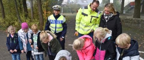 Junge Kinder sprühen eine Schablone mit Fußabdrücken mit Farbe voll. Im Hintergrund Polizisten