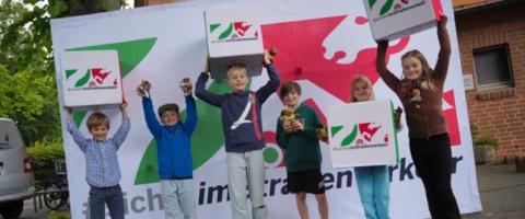 Schulkinder vor einer Wand mit dem Logo der NRW Initiative - #sicherimStraßenverkehr