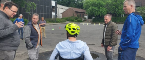 Ein Rollstuhlfahrer auf einer Rampe, daneben weitere Übungsteilnehmende