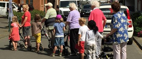 Seniorinnen und Seniorinnen gehen in Begleitung von Kindern über eine Straße