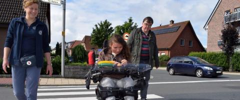 Eine Rollstuhlfahrerin überquert in Begleitung einen Zebrastreifen