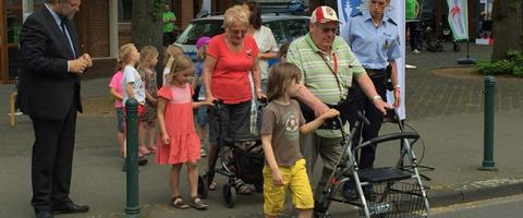 Seniorinnen und Senioren überqueren eine Straße. Kinder und Polizisten begleiten