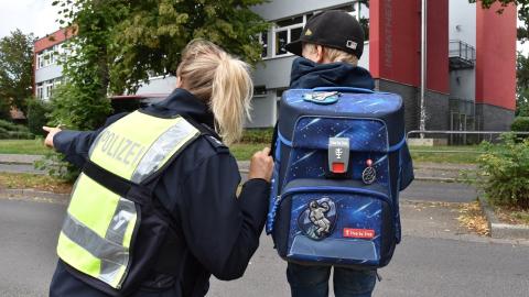 Ein Schulkind steht neben einer Polizistin. Die Polizistin zeigt nach links vorne