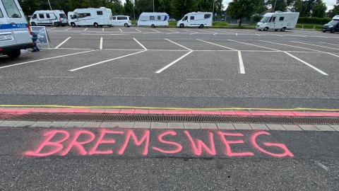 Auf einer Straße ist das Wort "Bremsweg" aufgesprüht. Im Hintergrund sieht man Campingwagen