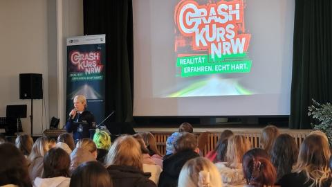 Ein Bild einer Crash-Kurs-Veranstaltung mit Zuschauern und einer Leinwand im Hintergrund. Auf dieser ist das Logo der Veranstaltung zu sehen