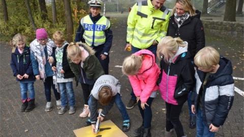 Ein Schüler sprüht mit gelber Farbe auf eine Schablone; diese zeigt einen Fuß. Im Hintergrund stehen weitere Schüler sowie Polizisten