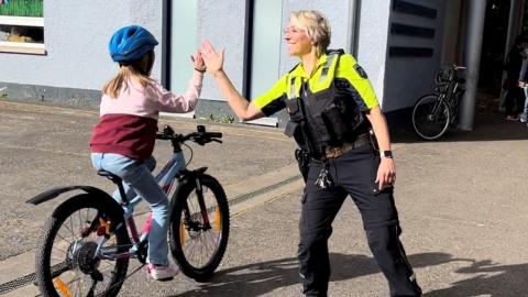 Eine Polizistin schlägt sich mit einem Kind auf einem Fahrrad per Handschlag ab