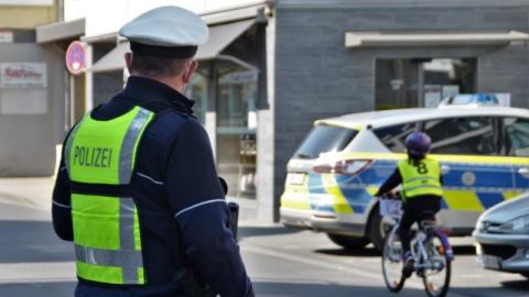 Ein Polizist in Uniform schaut einem Kind auf einem Fahrrad hinterher. Das Kind trägt eine gelbe Warnweste