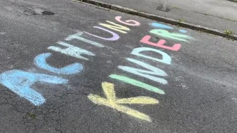 Auf einer Straße ist mit farbiger Kreide der Schriftzug "Achtung Kinder!" aufgebracht worden