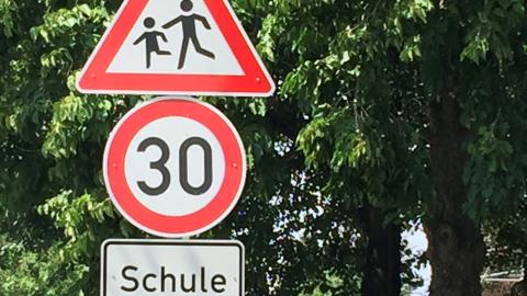 Drei Straßenschilder auf einem Schildmast. Oben ein rot umrandetes Dreieck mit laufenden Kindern. In der Mitte eine Tempobegrenzung auf 30 km/H. Unten der Hinweis "Schule"