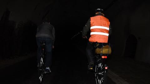 Zwei Personen fahren in der Dunkelheit Fahrrad. Der linke hat normale, dunkle Kleidung an, der rechte hat reflektierende Kleidung an und ist dadurch deutlich besser zu erkennen
