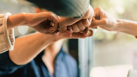 Mehrere Hände kommen in der Bildmitte als Faust zusammen