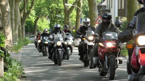 Ausfahrt einer Motorradgruppe entlang einer bewaldeten Straße