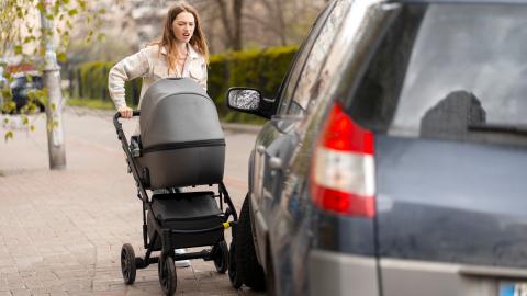 Ein geparktes Fahrzeug blockiert den Fußweg, eine Frau mit Kinderwagen kann nicht passieren