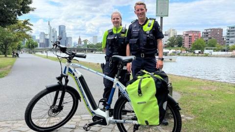 Polizisten vor einem Fahrrad an einem Flussufer