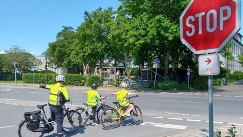 Kinder und ein Polizist an einer Stoppstraße auf dem Fahrrad