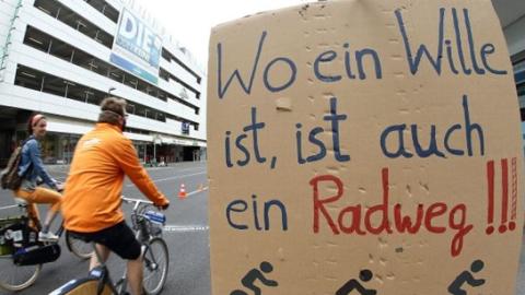 Radfahrende und ein Hinweisschild zu einer Demonstration