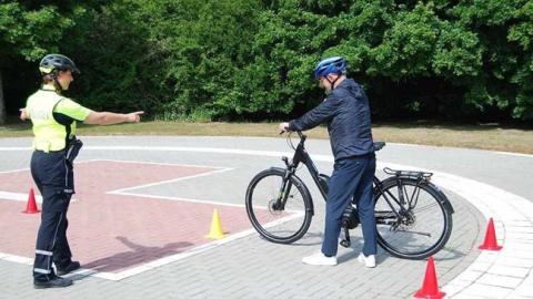 Ein Erwachsener mit Fahrrad erhält Anweisungen einer Polizistin