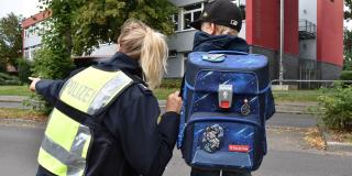 Ein Schulkind steht neben einer Polizistin. Die Polizistin zeigt nach links vorne