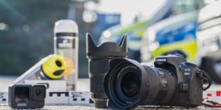 Eine Fotokamera liegt auf der Straße. Links und rechts liegen Materialen zur Unfallaufnahme der Polizei