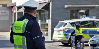 Ein Polizist in Uniform schaut einem Kind auf einem Fahrrad hinterher. Das Kind trägt eine gelbe Warnweste