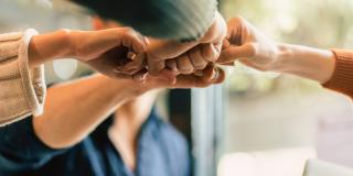 Mehrere Hände kommen in der Bildmitte als Faust zusammen